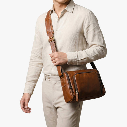 Sacoche en cuir cognac Tate portée en bandoulière croisée par un homme en chemise lin beige – Nord Brut